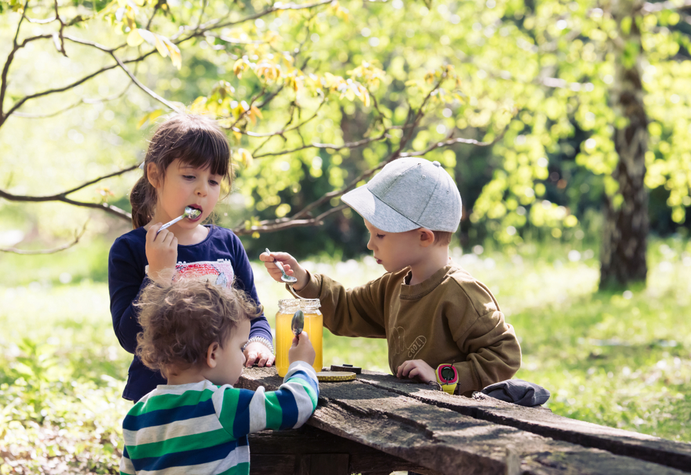 three children eating honey at a park